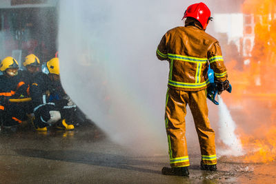 Rear view of firefighter spraying water on fire while standing at street