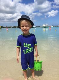 Portrait of cute boy standing in sea against sky