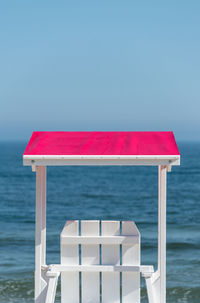 White lifeguard chair visible from the back with a pink visor against the background beautiful sea