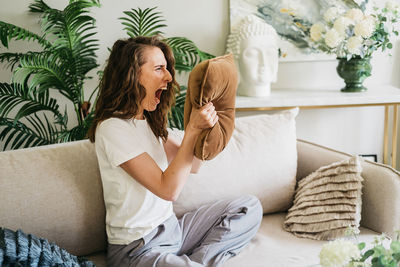 An angry woman screams into a pillow and slams her fists on the couch.