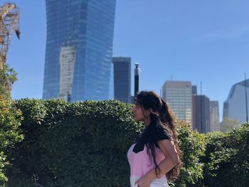 Woman standing by modern buildings against blue sky