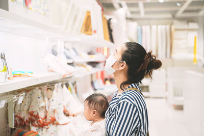 Side view of mother wearing mask with baby girl in store