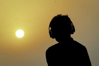 Silhouette man wearing headphones against orange sky