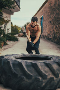 Young sportsman hitting tire with sledgehammer on street