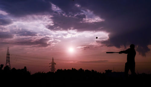 Silhouette man playing baseball against sky during sunset