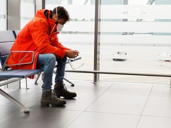 Man wearing mask using phone sitting on seat indoors