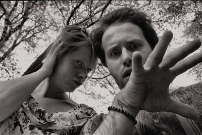 Portrait of man and woman gesturing against trees