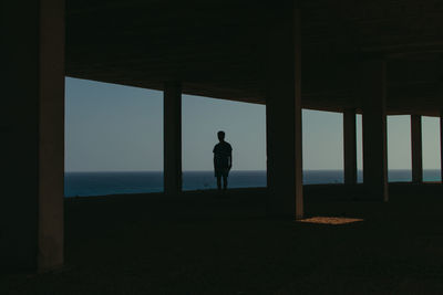 Silhouette man standing by window while looking at sea