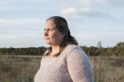 Mature woman looking away while standing on field against sky