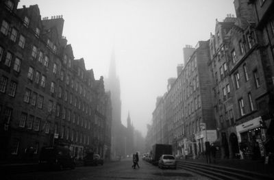 Street amidst buildings against sky in foggy weather
