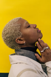 Side view of contemplating young female with eyes closed standing against yellow background