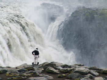 Rear view of man standing on rock against waterfall