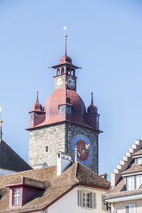 Low angle view of clock tower amidst buildings against clear blue sky