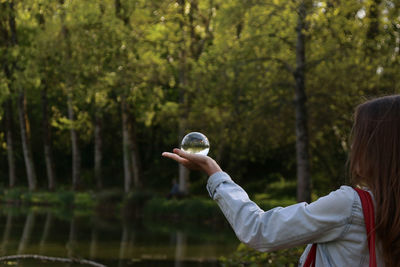 Side view of woman holding crystal ball while standing by lake