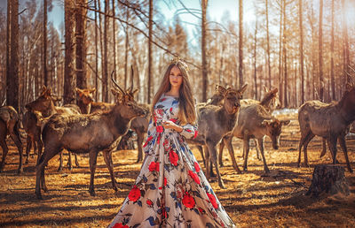 Portrait of young woman standing against deer at forest