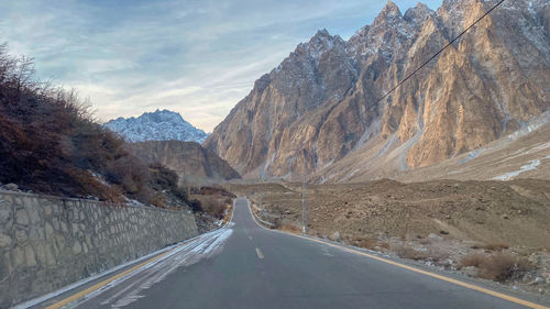 Empty road amidst snowcapped mountains against sky