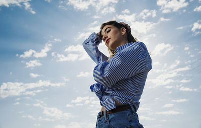 Low angle view of young woman standing against sky