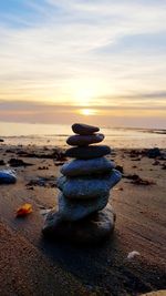 Stack of pebbles on beach against sky during sunset