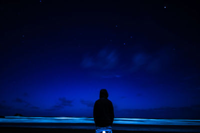 Rear view of silhouette man standing against sky at night