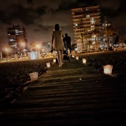 Rear view of people walking on illuminated street at night