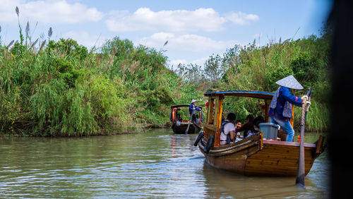 People sitting on riverbank against sky