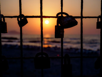 Close-up of padlocks on railing against sky during sunset