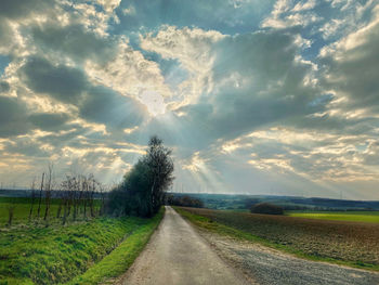 Dirt road amidst field against sky