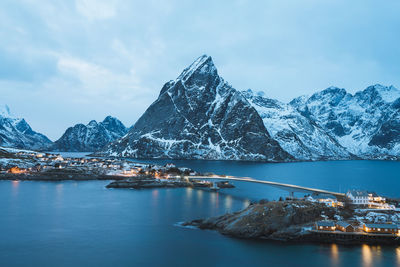 Scenic view of sea and snowcapped mountains against cloudy sky during sunset