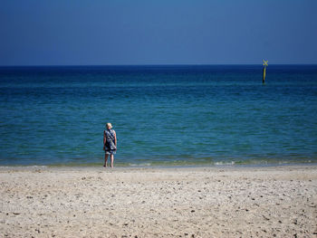Full length of man walking on beach against clear blue sky