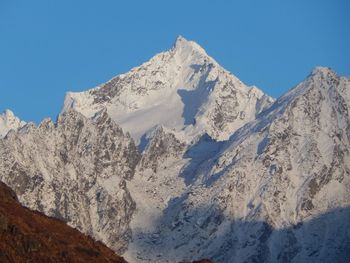 Low angle view of snowcapped mountains against clear blue sky