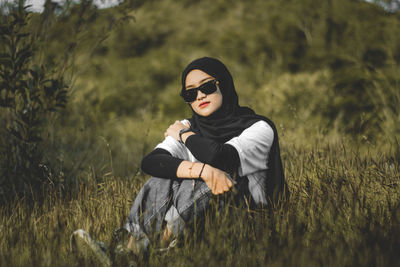 Young muslim woman wearing sunglasses sitting on field