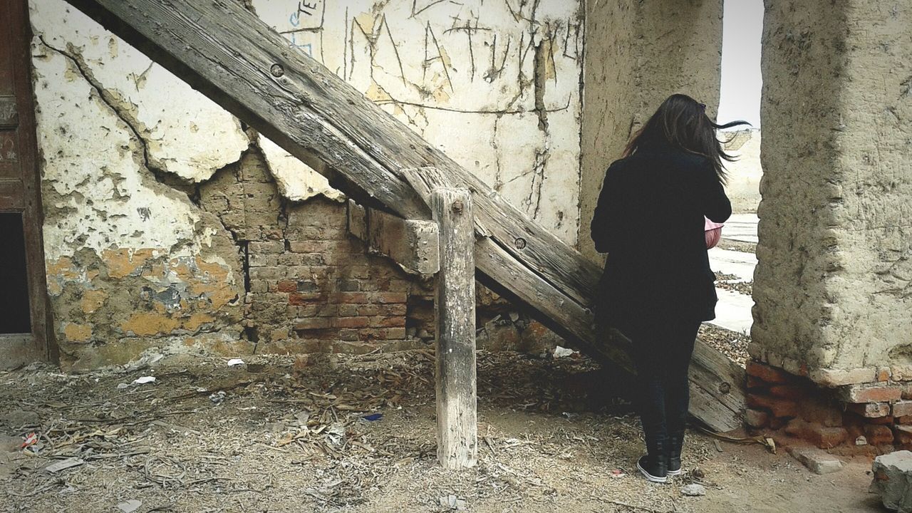 SIDE VIEW OF WOMAN STANDING BY BUILDING