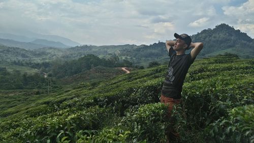 Young man standing on farm against cloudy sky
