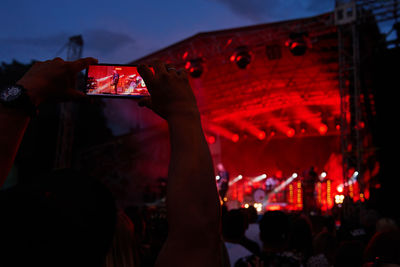 Person standing in front of stage, recording live music concert on smartphone