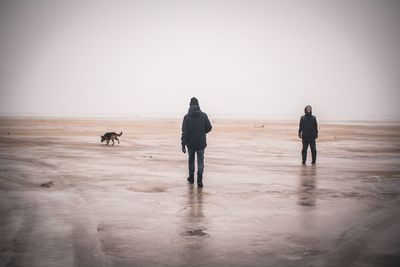 People walking at beach against clear sky