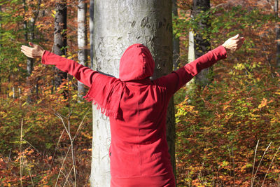 Rear view of man standing by tree trunk in forest