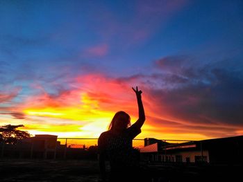 Silhouette woman photographing against orange sky