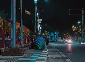 Rear view of man sitting on illuminated street at night