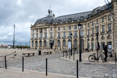 Side view of girl next to building against cloudy sky