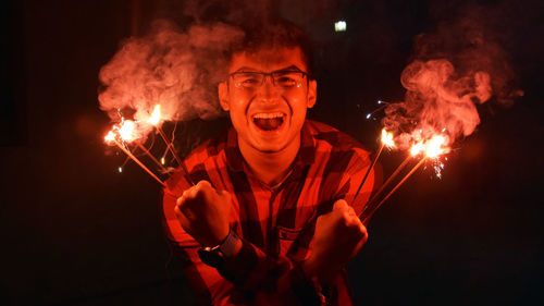 Portrait of happy man holding lit sparklers against black background