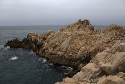 Rocks on shore by sea against sky