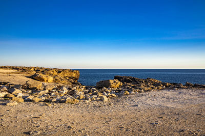 Scenic view of rocky beach against blue sky