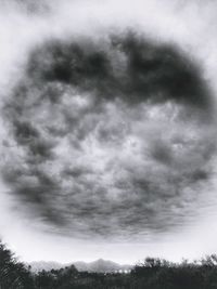 Low angle view of trees against cloudy sky