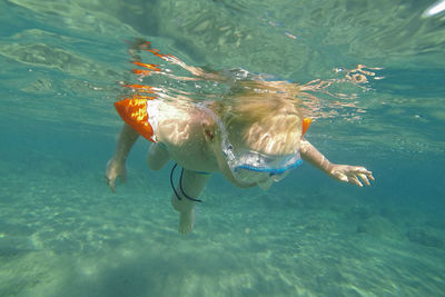 Child with floating muscles and water goggles swimming underwater