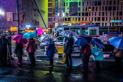 Rear view of people walking on wet illuminated city at night