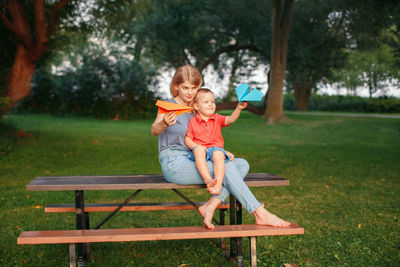 Smiling mother with boy sitting on bench in park