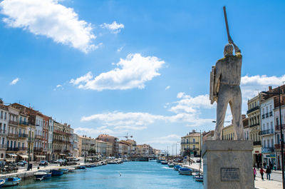 Statue by canal in city against sky