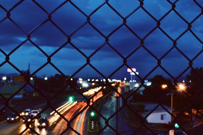 Illuminated cityscape seen through silhouette chainlink fence at night