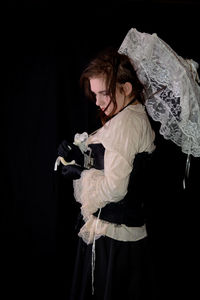 Young girl in steam punk look, holding white open umbrella, standing and looks down