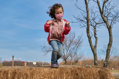 Girl in a mask having fun playing with haystacks at the county fair